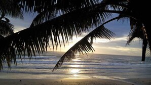 Escena de platja amb palmeres i el sol ponent sobre l'oceà.