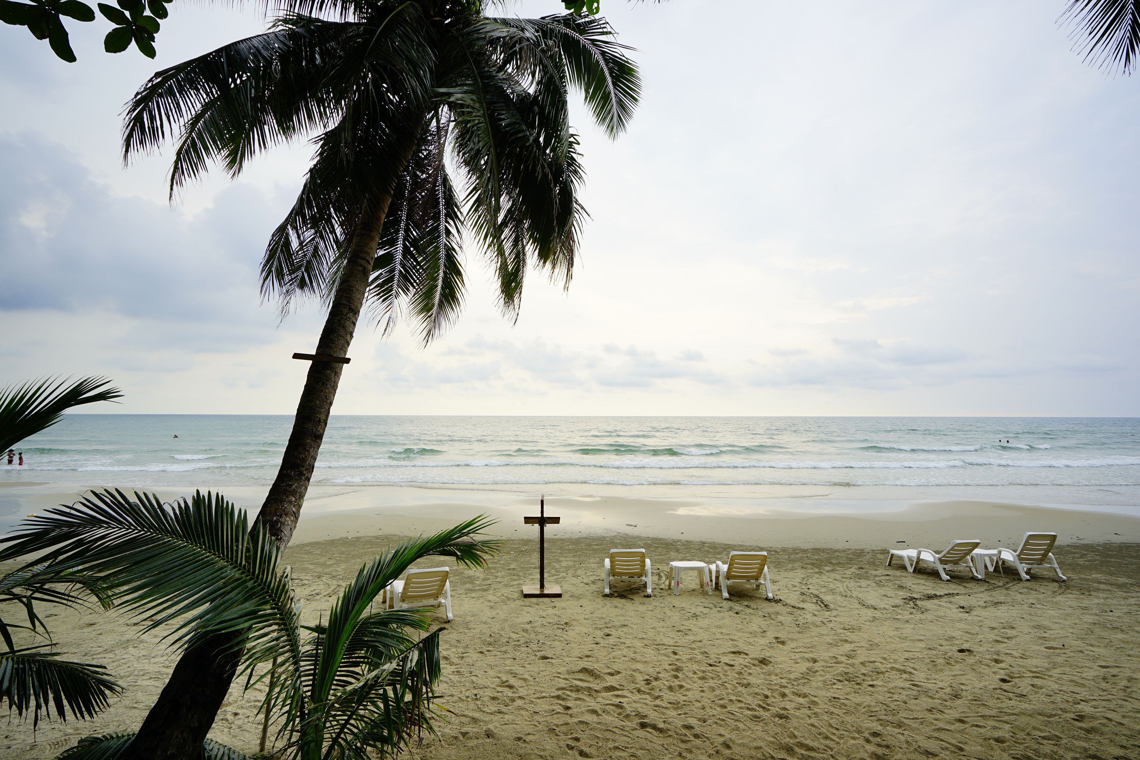 A beach with palm trees, a cross, and beach chairs.