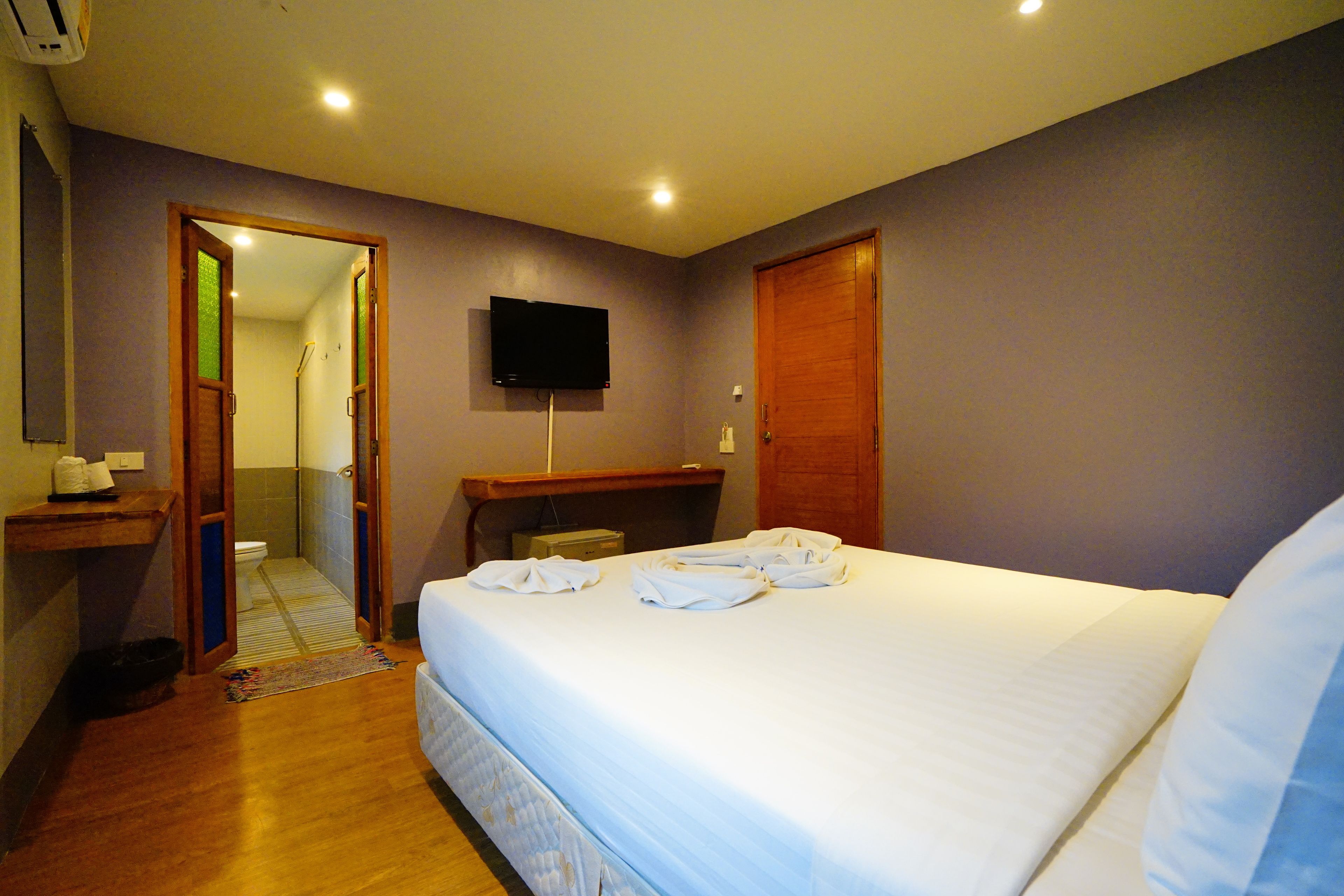 A hotel room with a bed, a television, a wooden desk, and a bathroom visible through an open door.