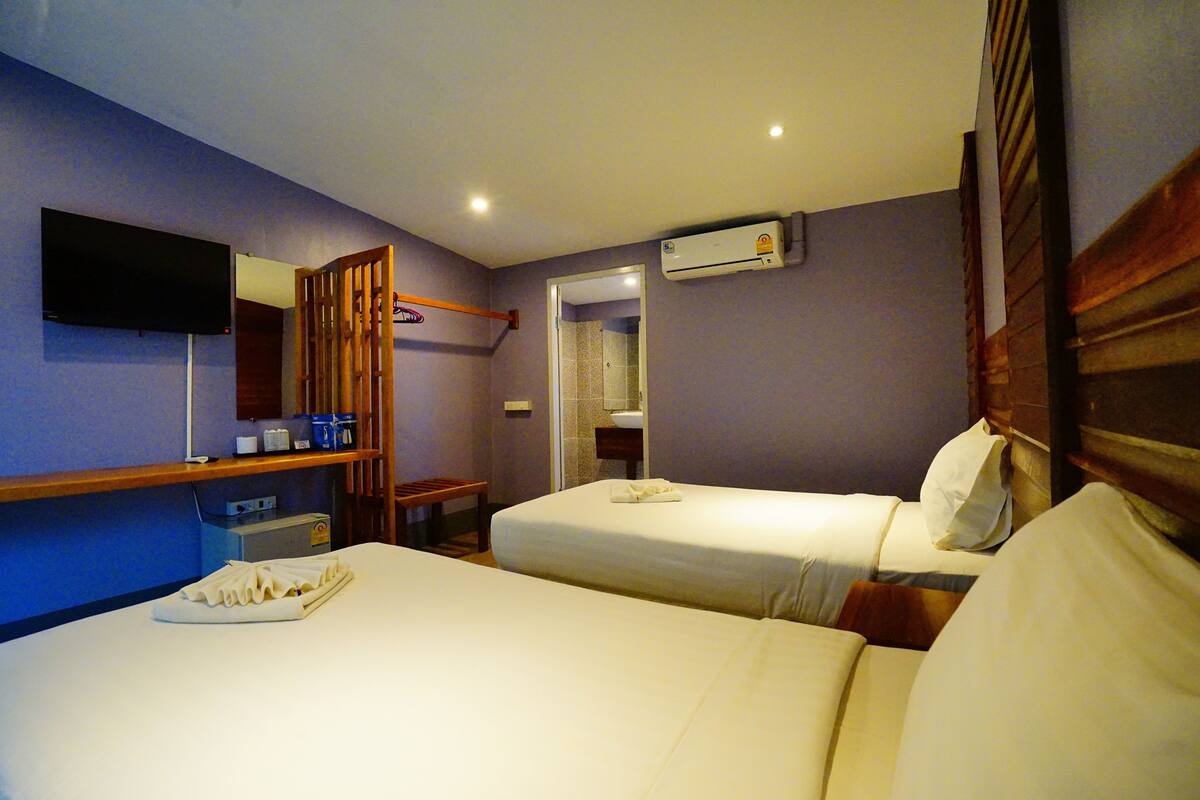 Ein Hotelzimmer mit zwei Betten, einem Fernseher, einer Klimaanlage und einem durchgegangenen Badezimmer.
