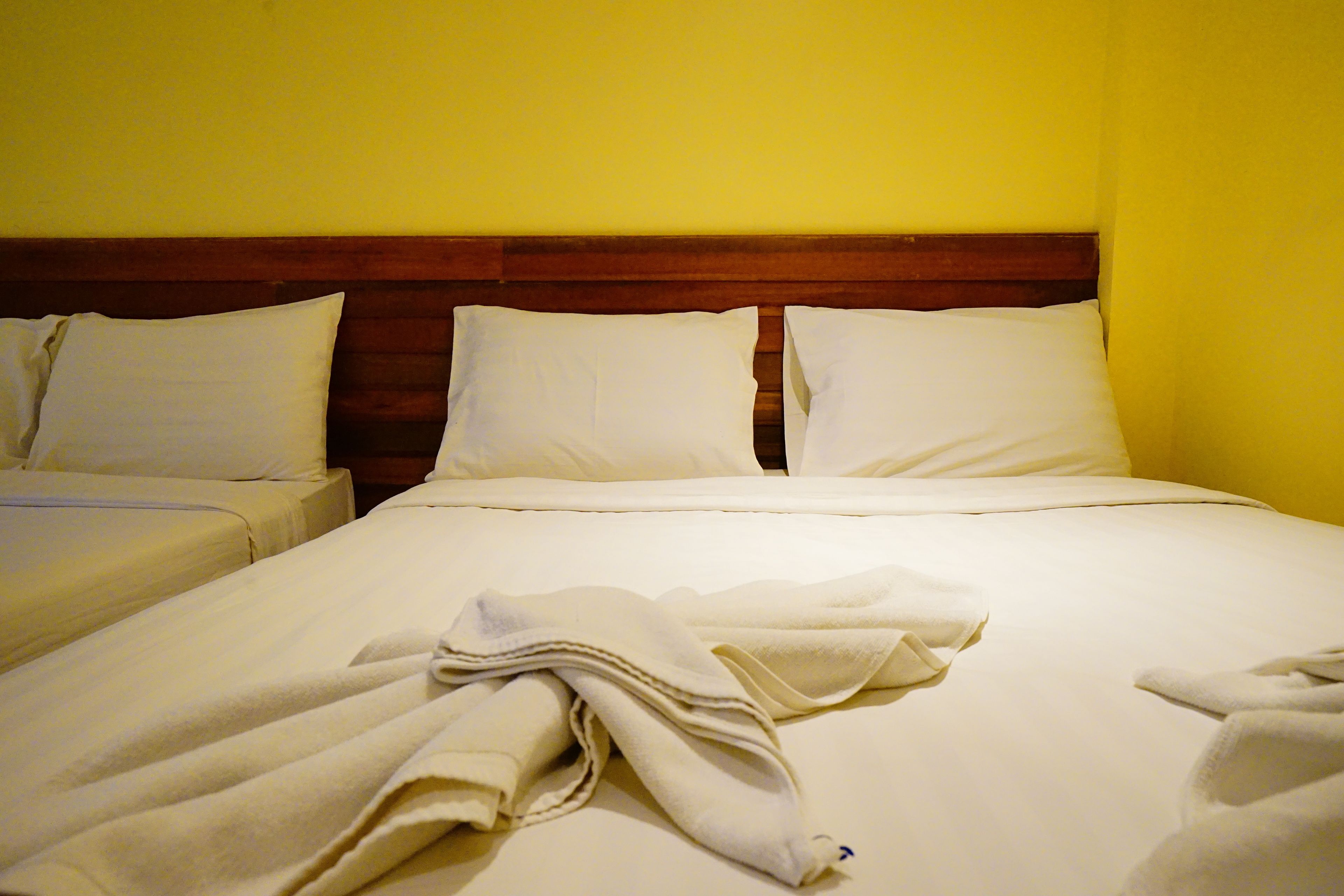A hotel room with two beds, wooden headboard, and plain yellow walls.