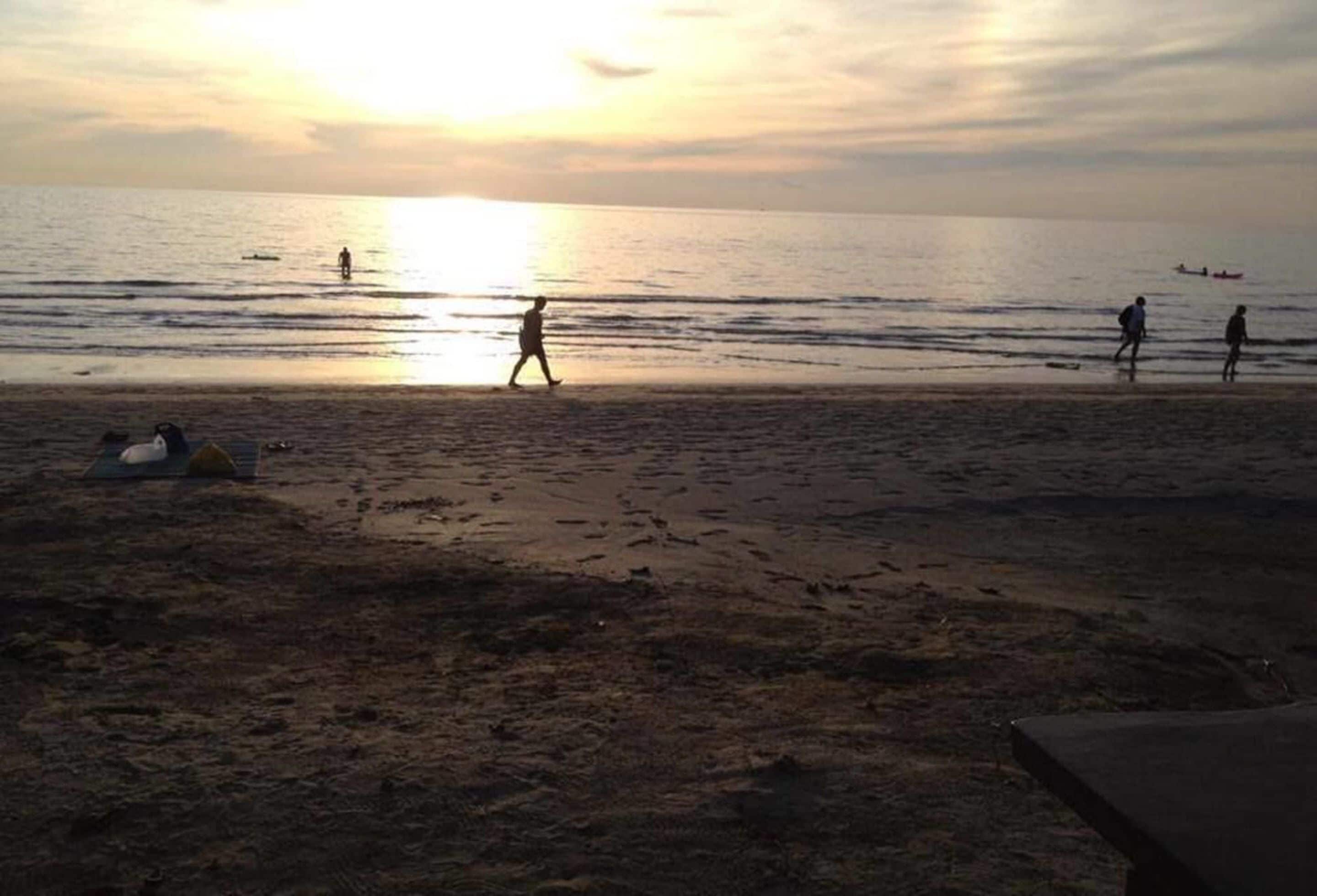 Escena de playa con gente caminando y un barco a lo lejos.
