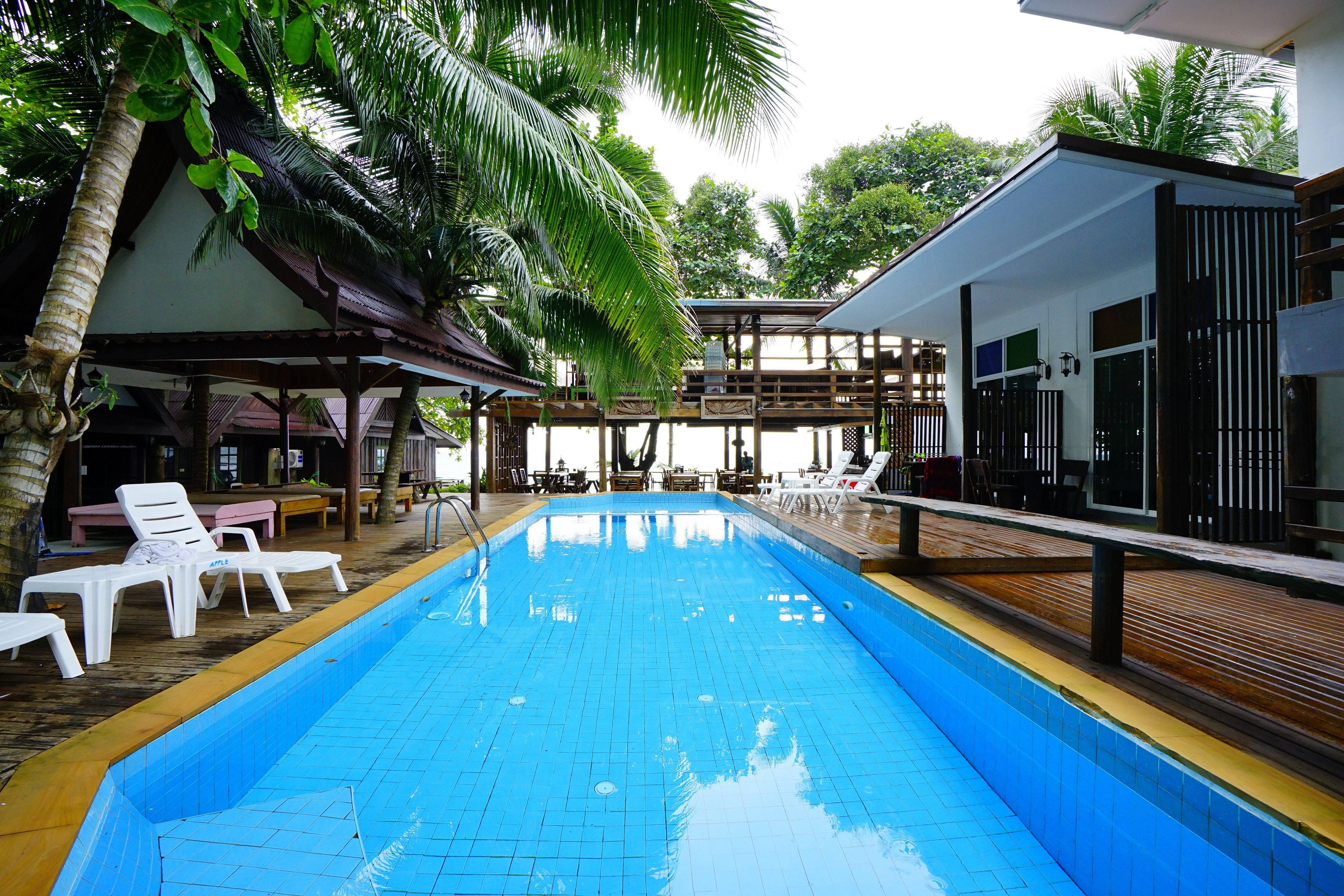 A swimming pool with lounge chairs and a covered area with tables and chairs.
