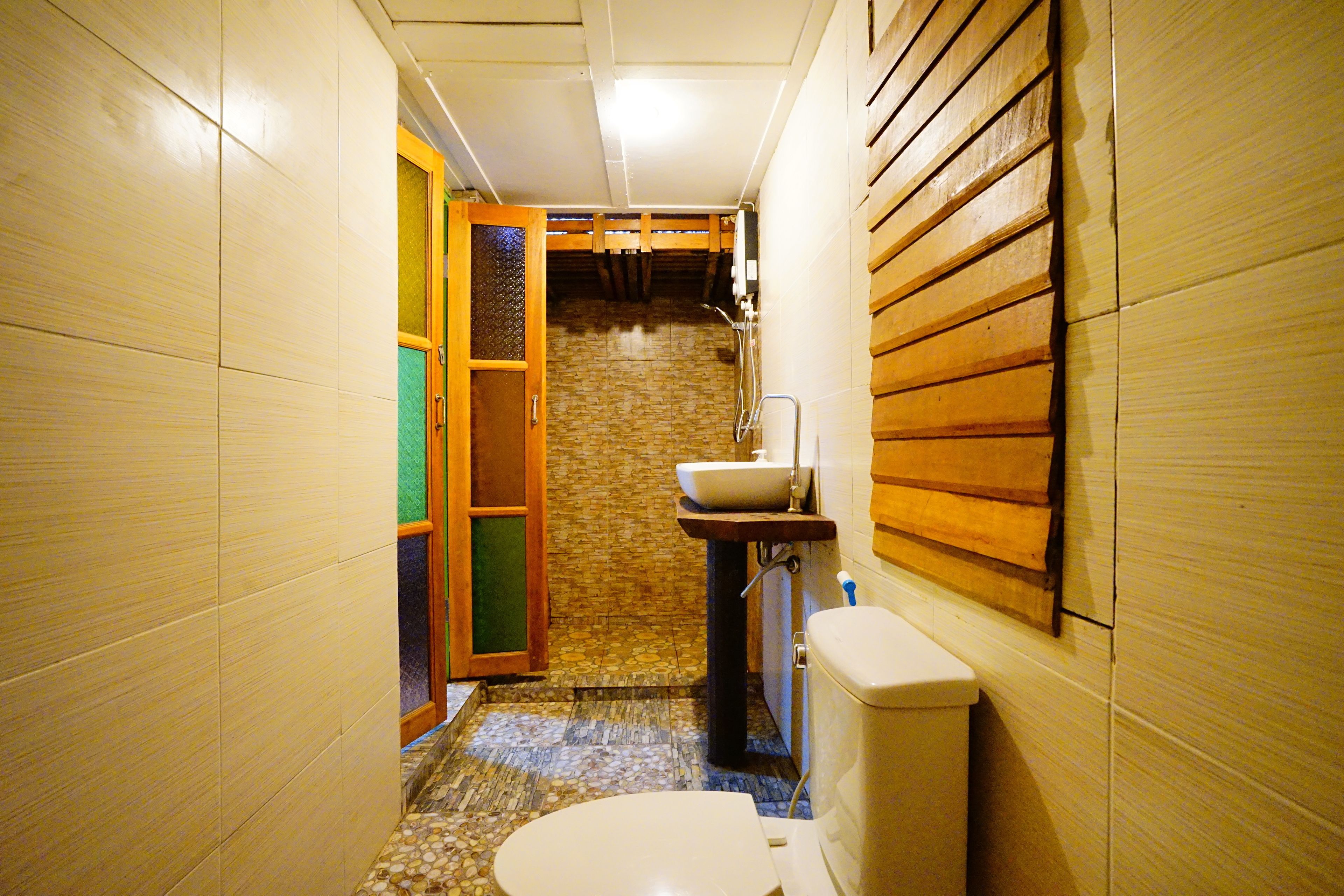 Un baño estrecho con inodoro, lavamanos y paneles de madera en las paredes.