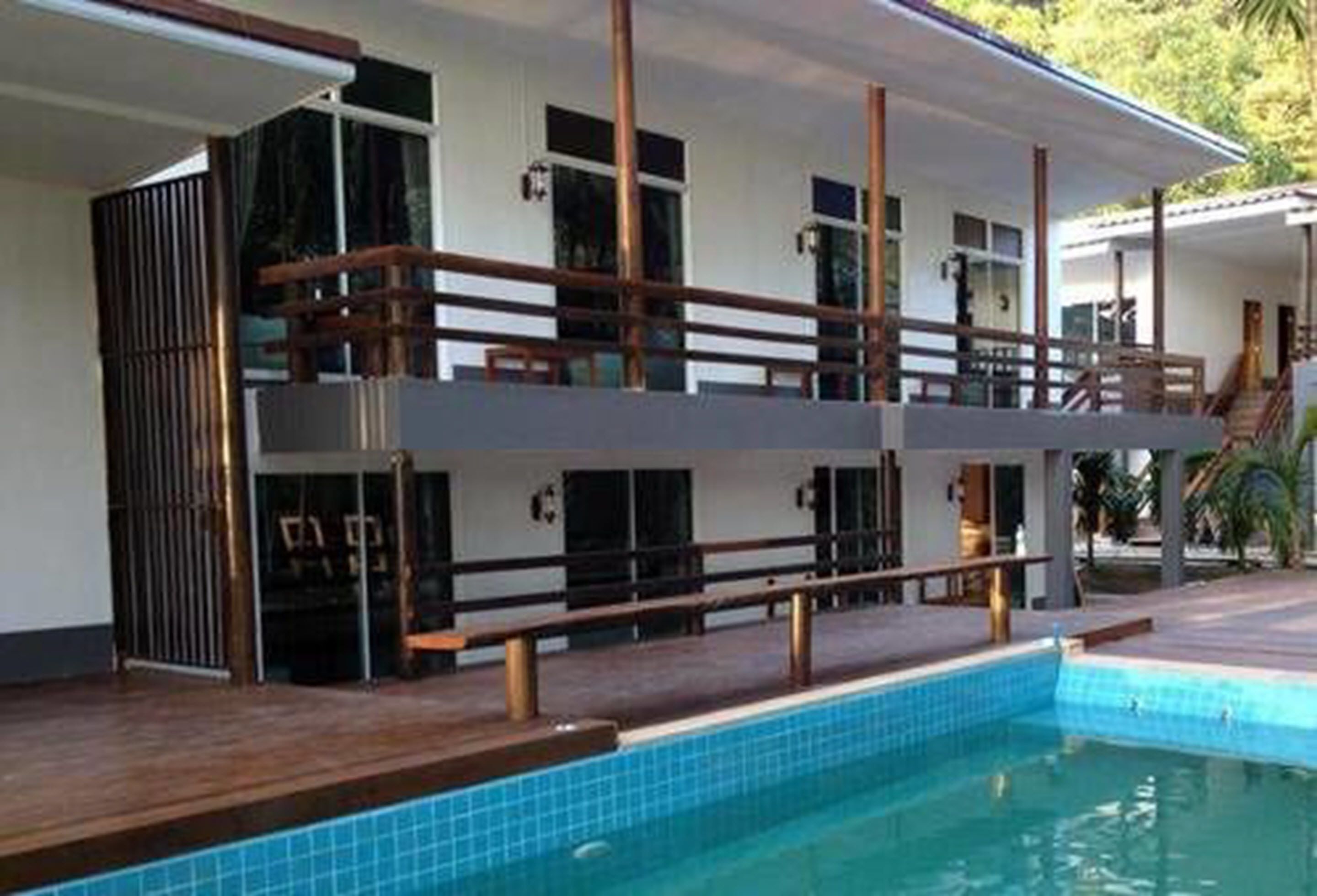 A two-story building with a swimming pool, wooden deck, and a covered area with a staircase.