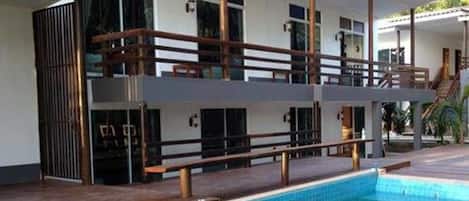 Ein zweistöckiges Gebäude mit Pool, Holzterrasse und überdachtem Bereich mit Treppe.