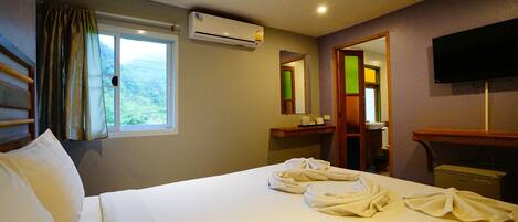 Quarto de hotel com cama, janela, ar condicionado, espelho, televisão e banheiro.