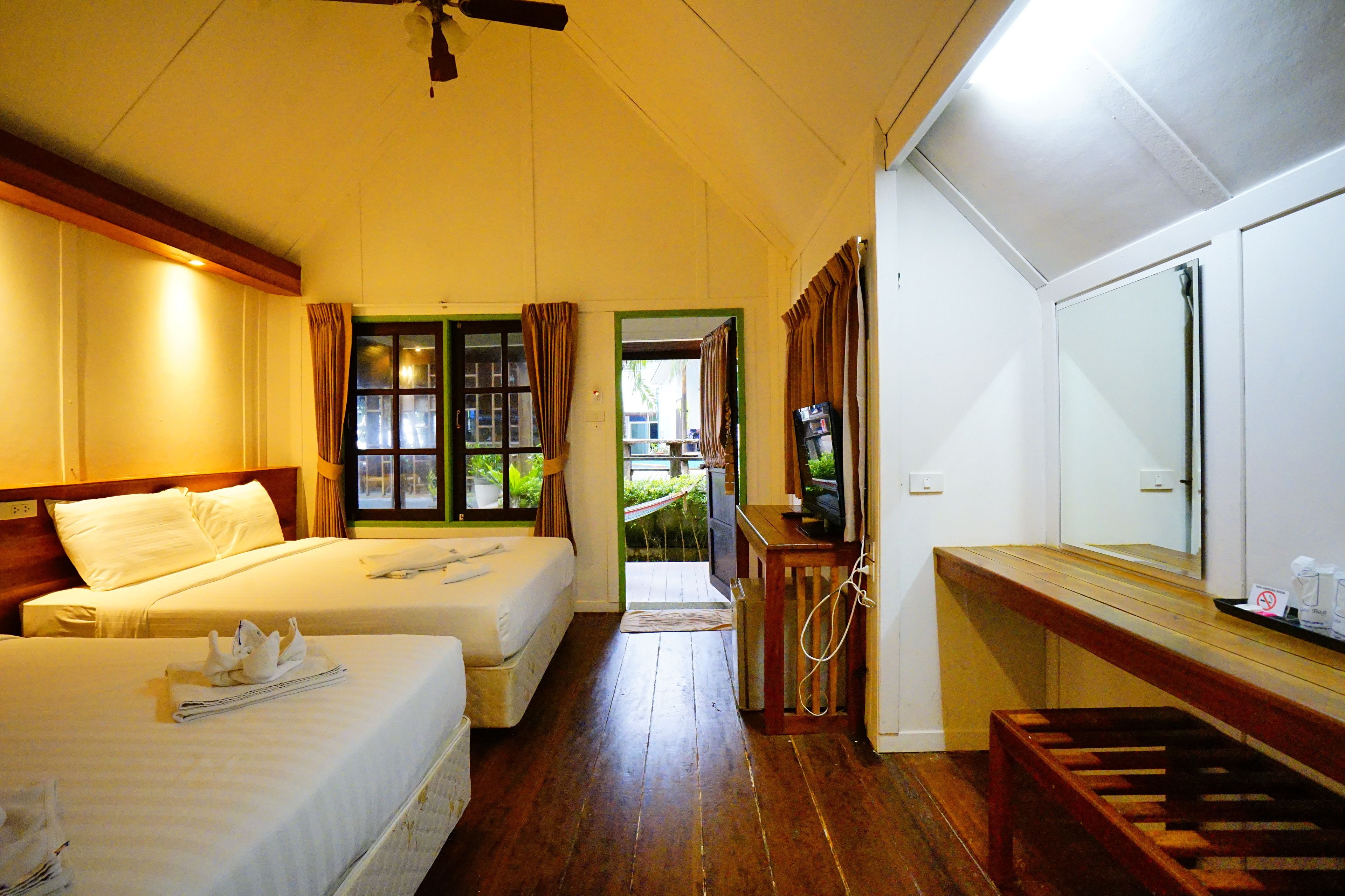 Habitación de hotel con dos camas, un banco de madera, un televisor y un baño con espejo.
