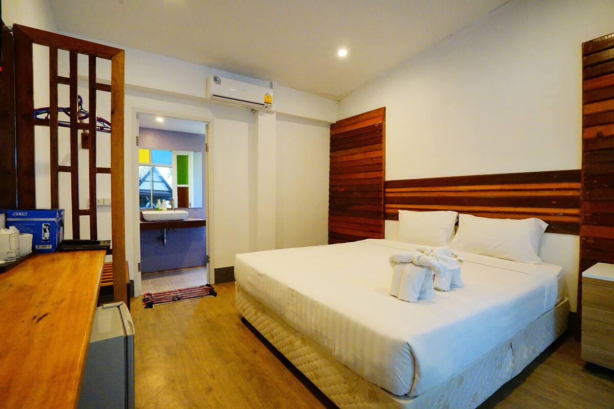 Ein Hotelzimmer mit Bett, Holz-Kopfteil, Schreibtisch mit Stuhl, einem kleinen Tisch und einem durchgegangene Tür erkennbaren Badezimmer.