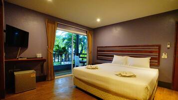 A hotel room with a large bed, a desk with a TV, and a sliding glass door to a balcony.