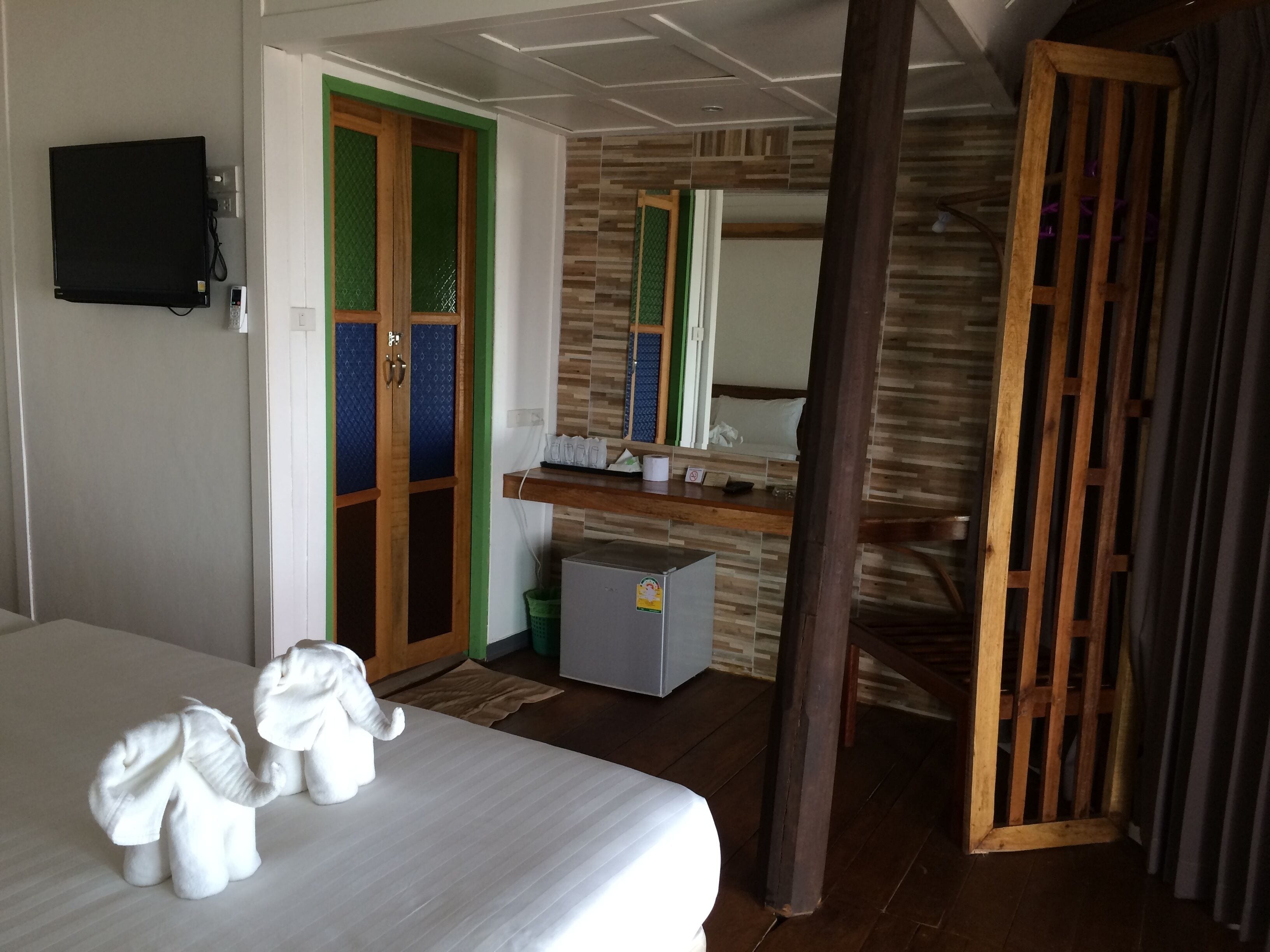 Une chambre d’hôtel avec un lit, un bureau, un miroir et une porte ornée de panneaux verts et bleus.