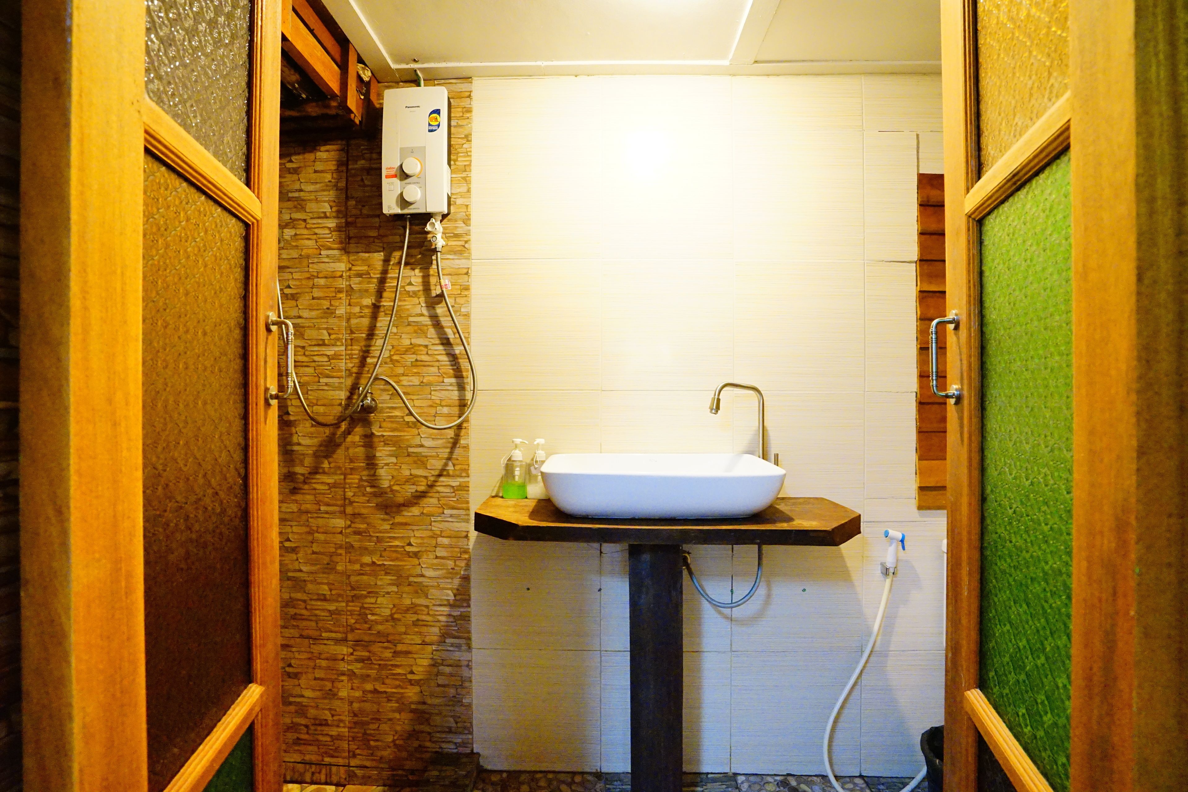A bathroom with a stone wall, a wooden vanity, a white sink, and a shower with a hose.
