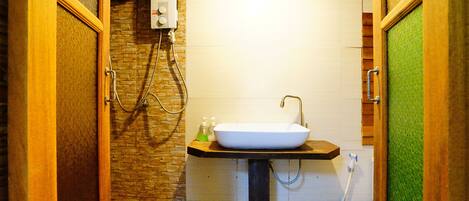 Un baño con pared de piedra, tocador de madera, lavamanos blanco y ducha con manguera.