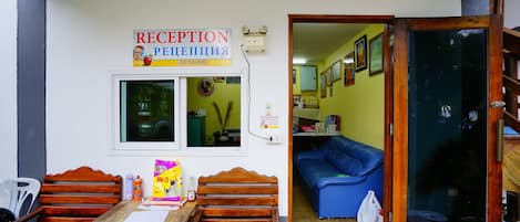 Un espace d’accueil comprenant un banc en bois, une table avec des documents, un canapé bleu et une porte vitrée donnant sur une pièce.