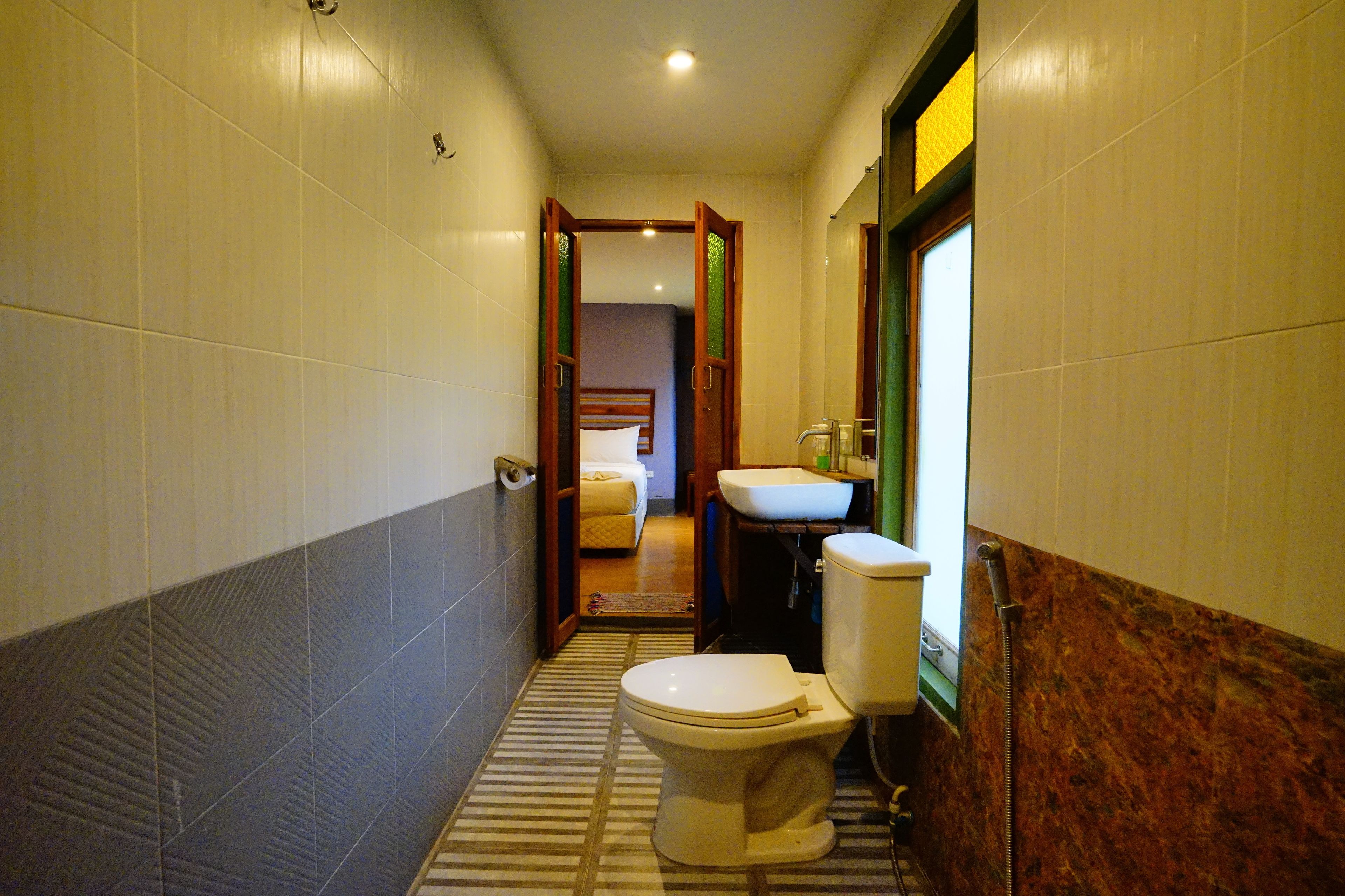 A narrow hallway with a toilet, sink, and a bed visible in the background.