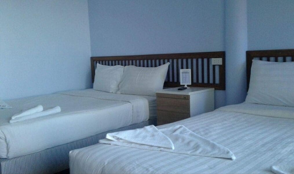 A hotel room with two beds, each with white linens and pillows. There is a wooden headboard, a nightstand with a lamp, and a small table with a remote control.