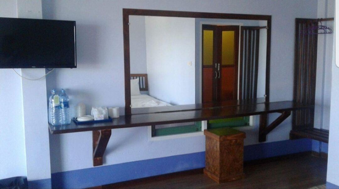 Una habitación con una cama, un televisor montado en la pared, una mesita con una botella de agua y un espejo que refleja una puerta y una ventana.