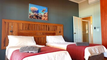 Habitación de hotel con dos camas, un cabecero de madera, un cuadro de tortugas marinas y una puerta a la derecha.