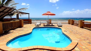 A swimming pool with a tiled edge, surrounded by lounge chairs and a table.