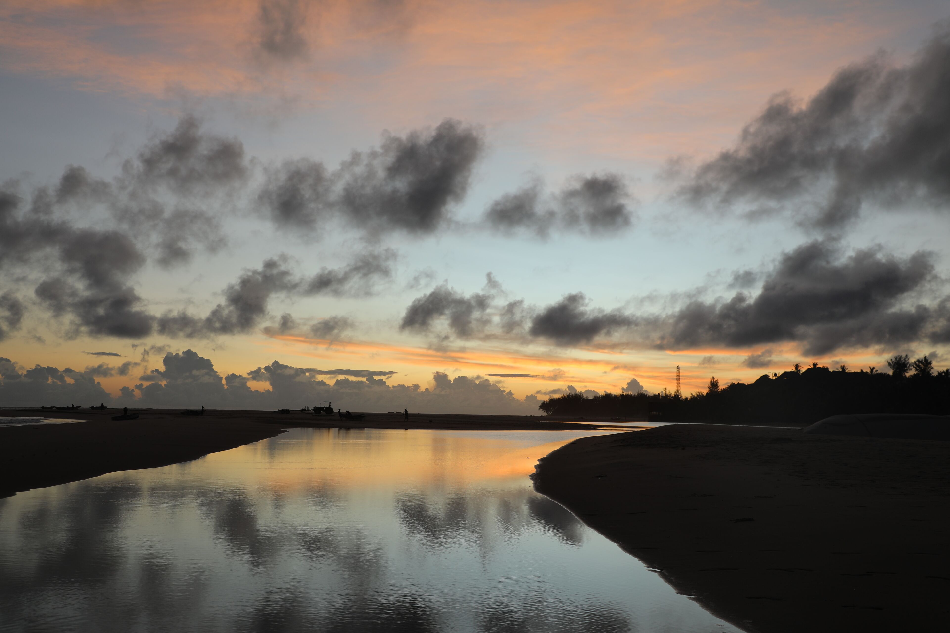 A calm beach with a reflective water surface, a clear sky, and distant landforms.