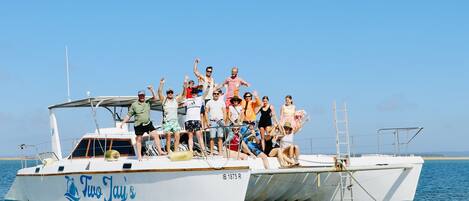 A boat named 'Two Jay's' with people on deck, a ladder, and a clear sky in the background.
