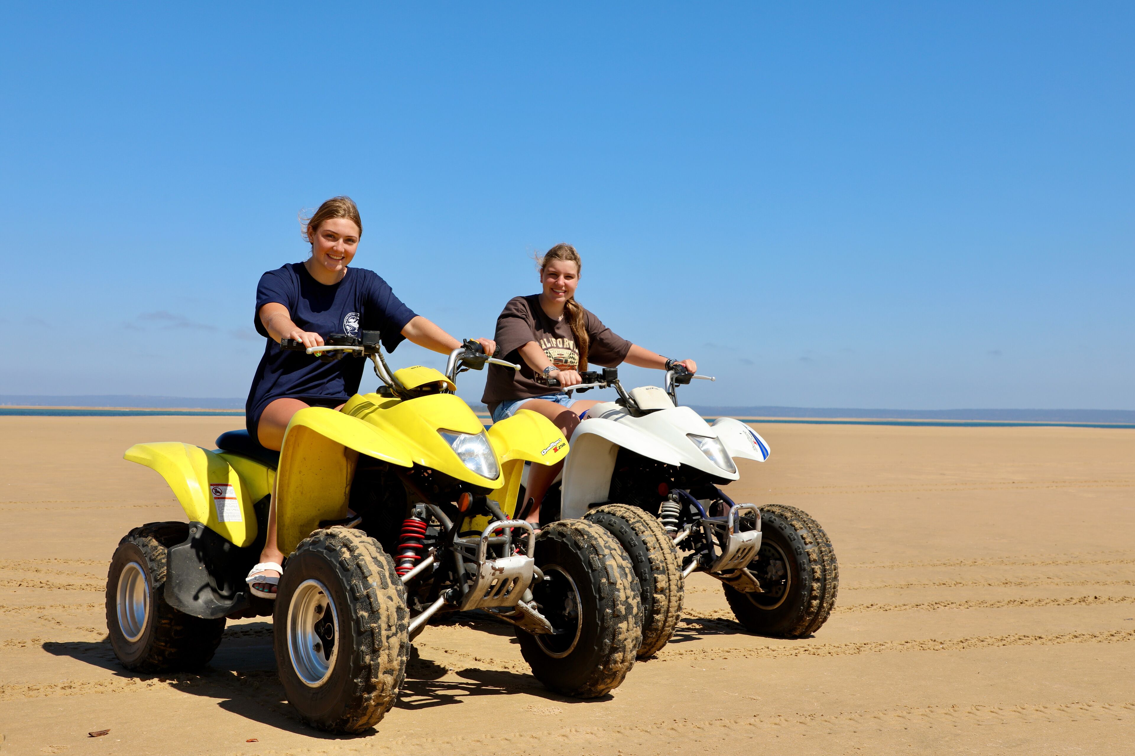 Two people on ATVs on a sandy beach.