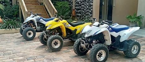 Three ATVs parked on a brick patio with a wooden staircase and plants in the background.