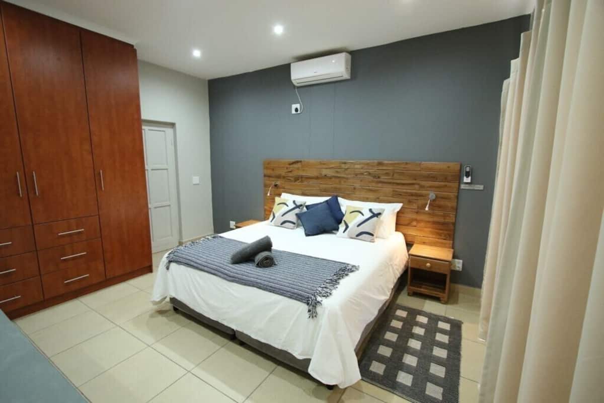 A bedroom with a wooden headboard, a bed with a white bedspread and blue pillows, a small bedside table, and a large wardrobe.