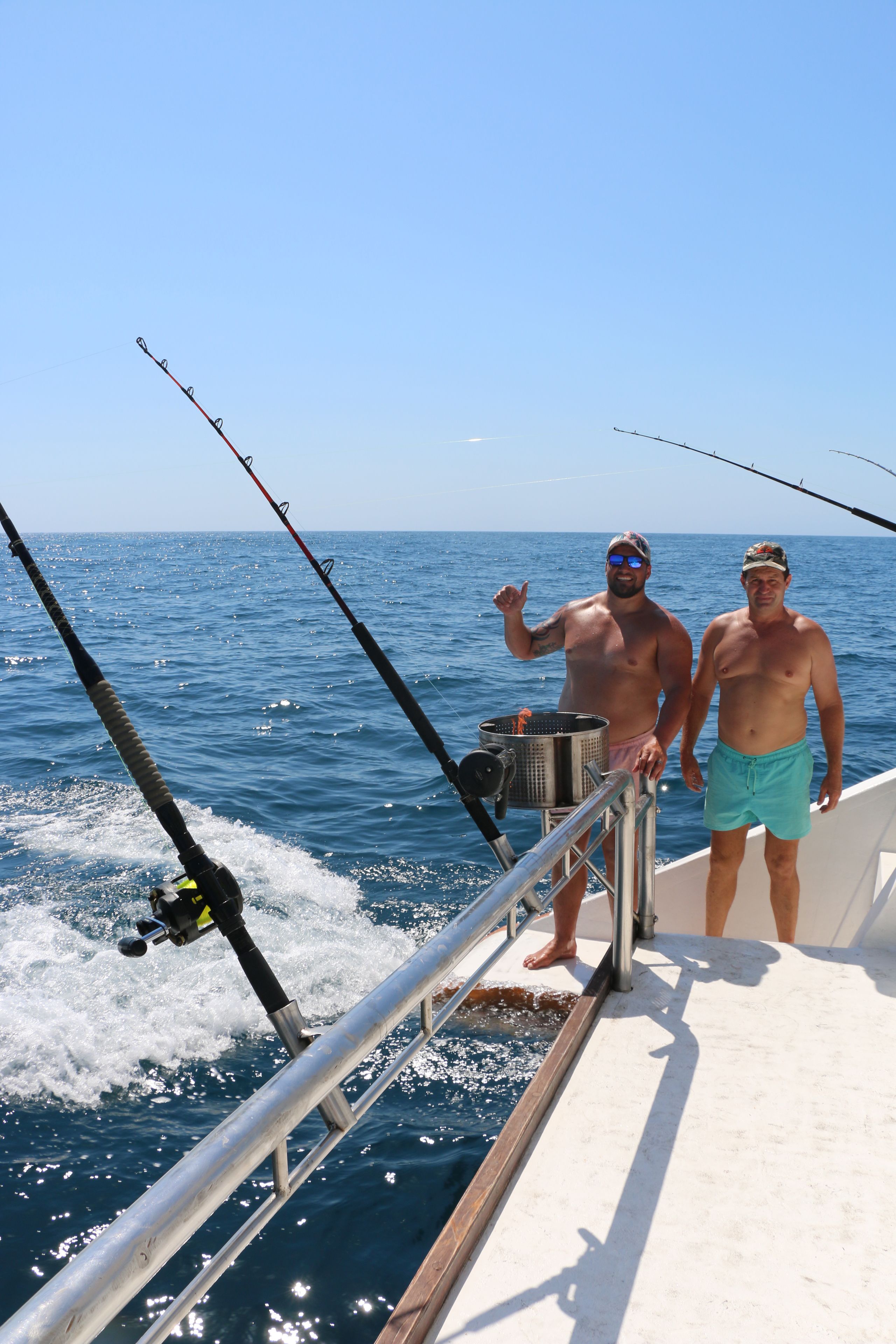 Due uomini su una barca con canne da pesca, una ringhiera metallica e l'oceano sullo sfondo.