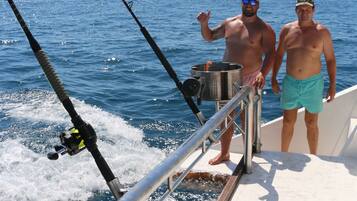 Due uomini su una barca con canne da pesca, una ringhiera metallica e l'oceano sullo sfondo.