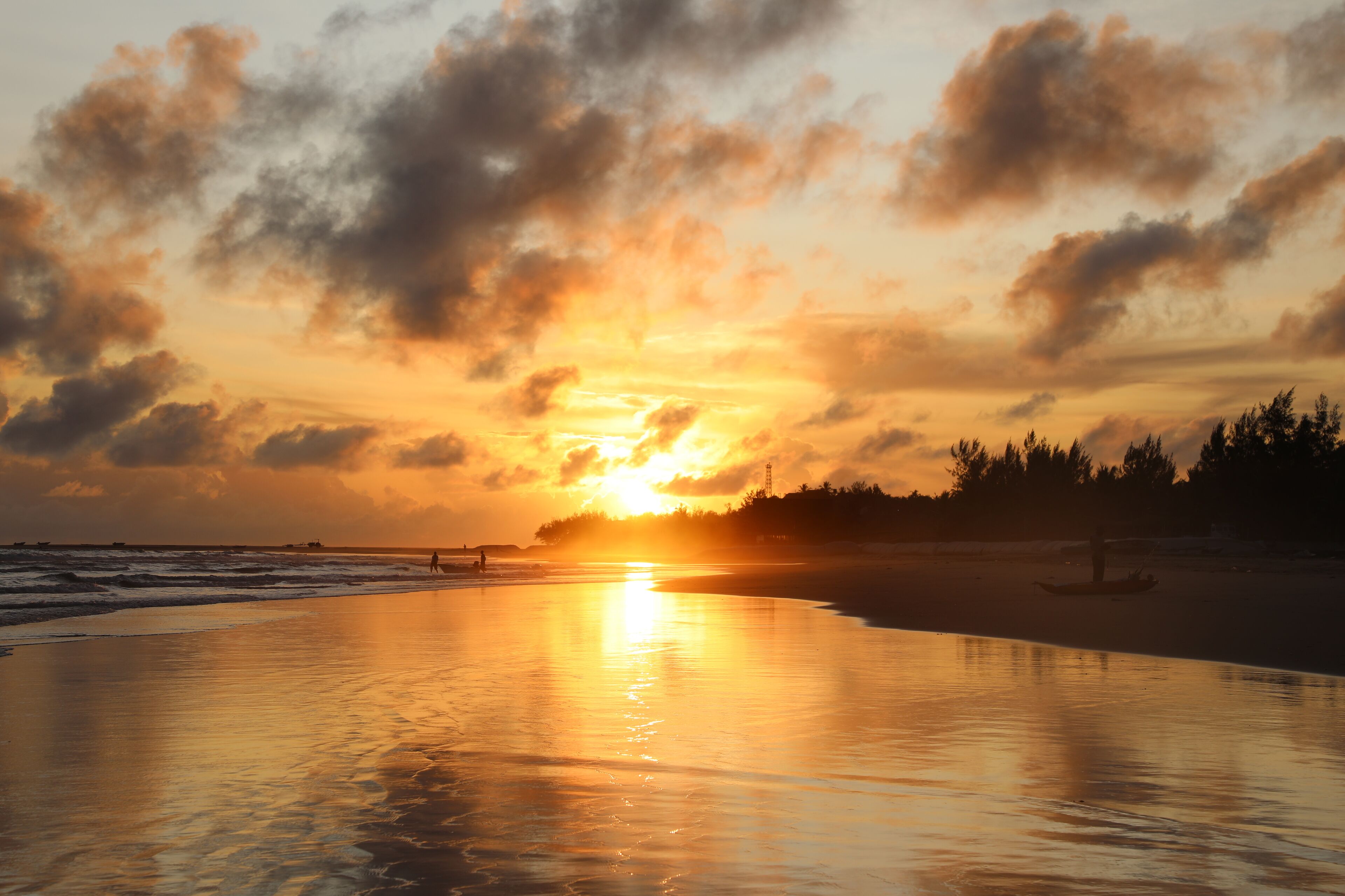 A beach scene with a sunset, calm sea, and a boat on the shore.