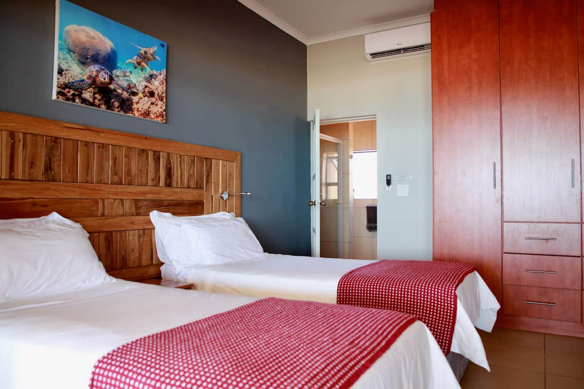 A hotel room with two beds, wooden headboard, a red and white checkered bedspread, a painting of a turtle on the wall, and a wooden wardrobe.