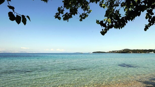 A clear view of a pebble beach leading to calm waters with a distant landmass. - Efi & Sofia Apartments (Corfu)