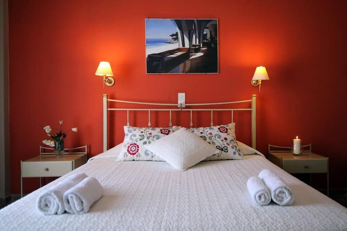 A neatly made bed with floral pillows, two bedside lamps, a framed picture above the bed, and a small table with a candle on the nightstand.