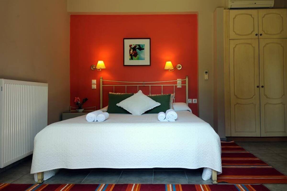 A hotel room with a bed, two bedside lamps, a radiator, a wardrobe, and a colorful striped rug.