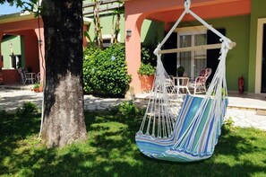 A hanging chair with a striped cushion in front of a building with a green and orange facade. - Efi & Sofia Apartments (Corfu)