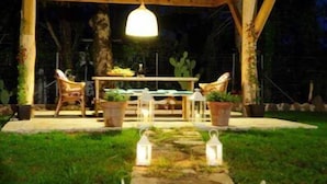 An outdoor patio area with a wooden pergola, stone pathway, and white lanterns. - Efi & Sofia Apartments (Corfu)