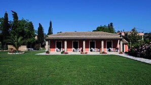 A building with a tiled roof and a covered porch with chairs. - Efi & Sofia Apartments (Corfu)