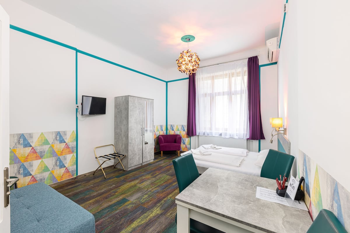 A modern hotel room with a bed, a desk with a chair, a TV, and a colorful geometric wall design.