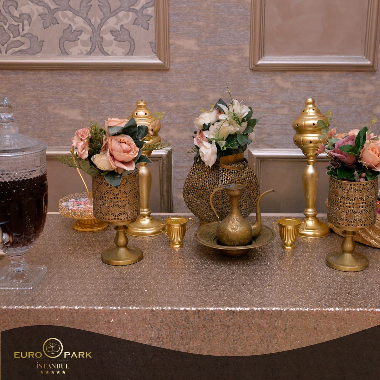 Une table ornée de décorations en laiton et de verrerie, comprenant des vases avec des fleurs et une théière, le tout posé sur un comptoir en marbre.