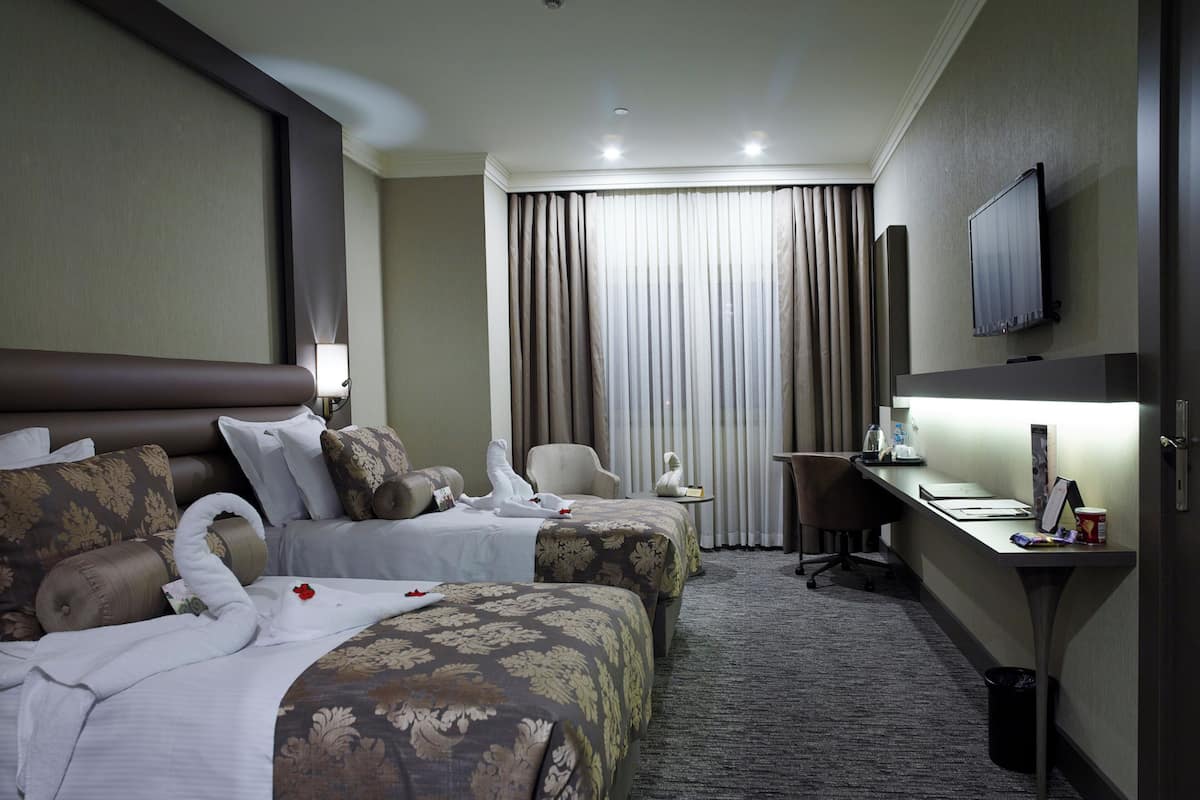 A hotel room with two beds, a desk, a chair, a TV, and a window with curtains.