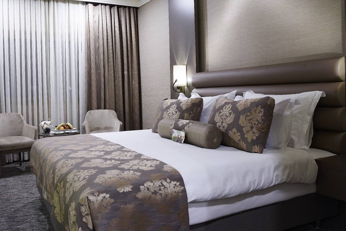 A hotel room with a large bed, a seating area with a chair and a small table, and a window with curtains.
