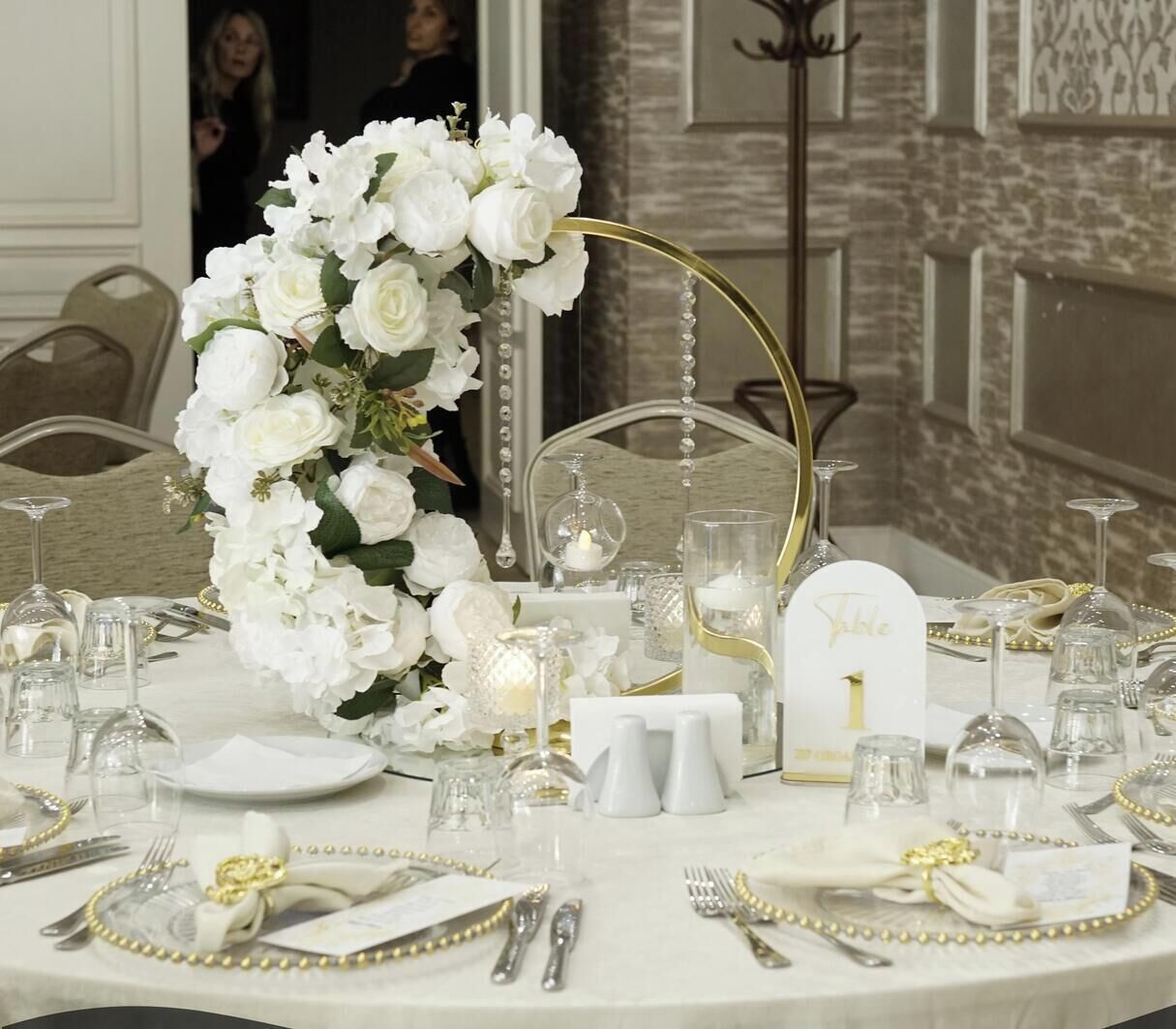 A table set for a formal event with white flowers, crystal glassware, and gold accents.