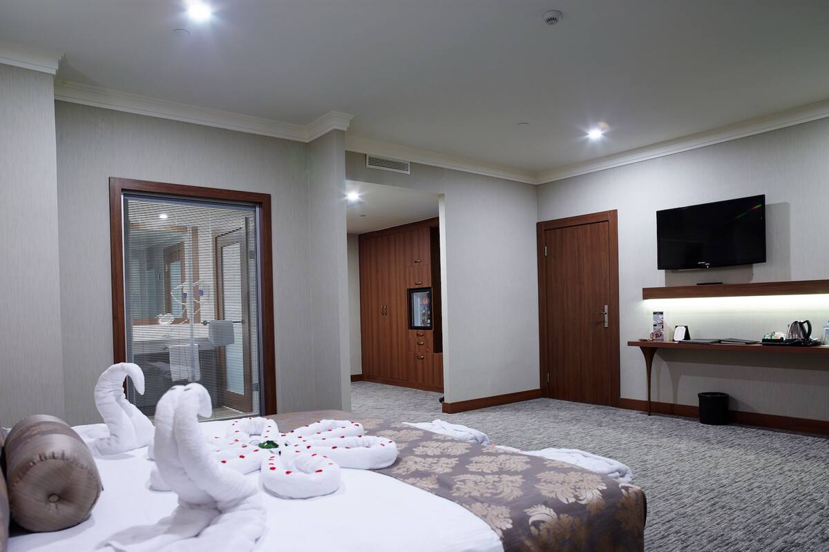A hotel room with a bed, a TV, a desk, and a bathroom visible through a glass door.