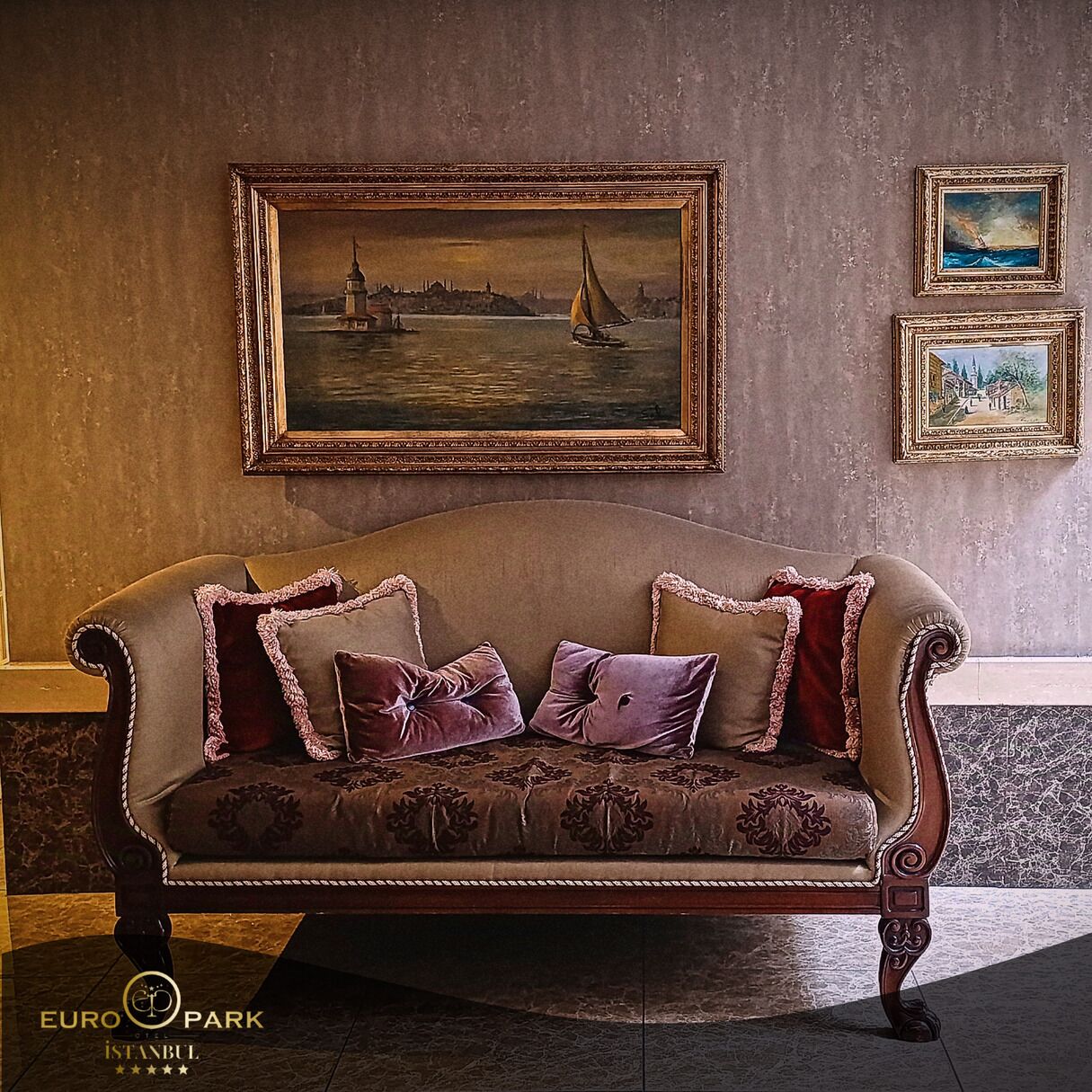 A vintage sofa with ornate carvings and tassels, positioned in a lobby with a large framed painting of a cityscape above it.