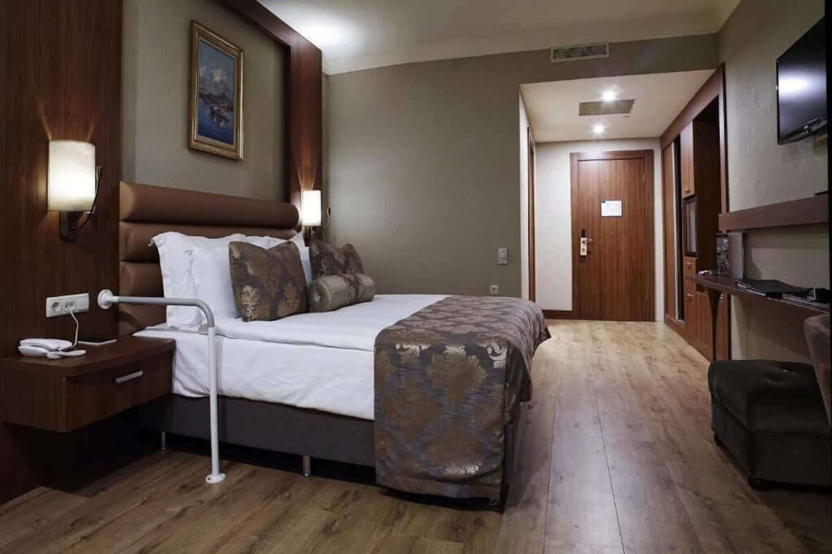 A hotel room with a bed, bedside table, lamp, and a television on the wall.