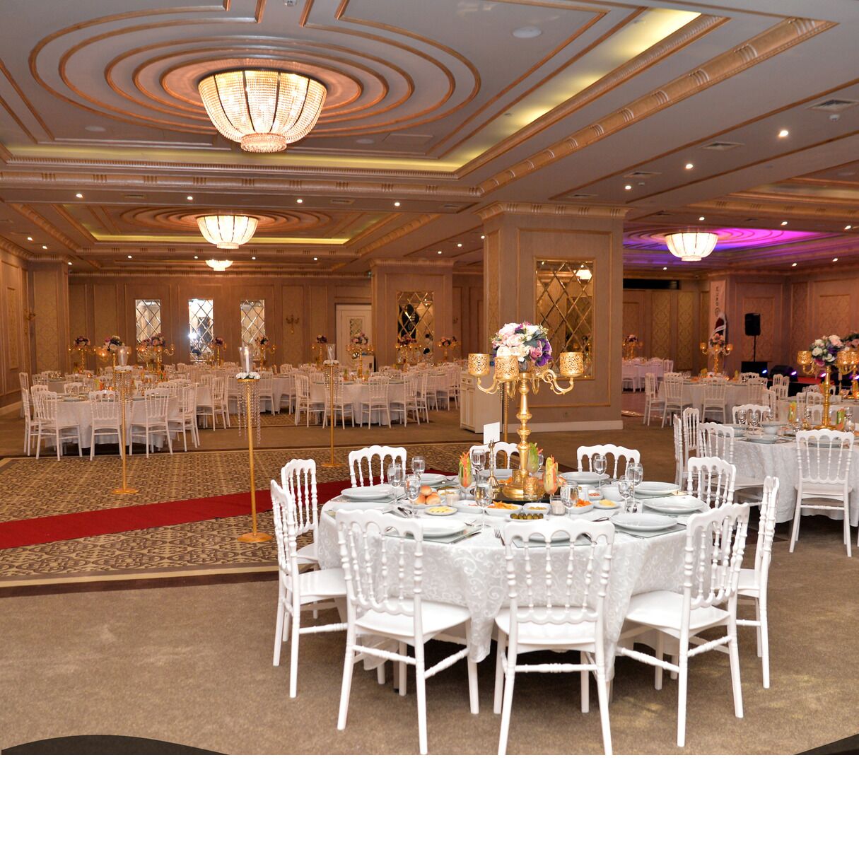 A banquet hall with round tables set for dining, white chairs, and chandeliers.