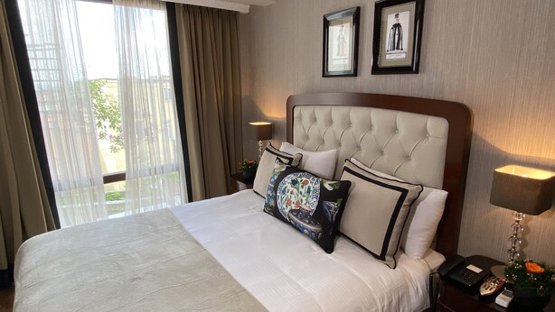 Habitación de hotel con una cama grande, una mesita de noche con lámpara y una ventana con cortinas.