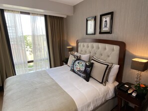 Habitación de hotel con una cama grande, una mesita de noche con lámpara y una ventana con cortinas.