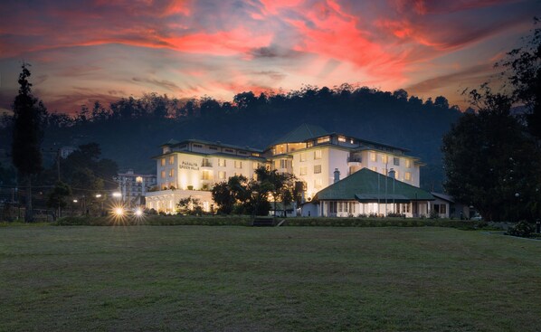 A large, multi-story hotel with a green roof, surrounded by a grassy area and trees.